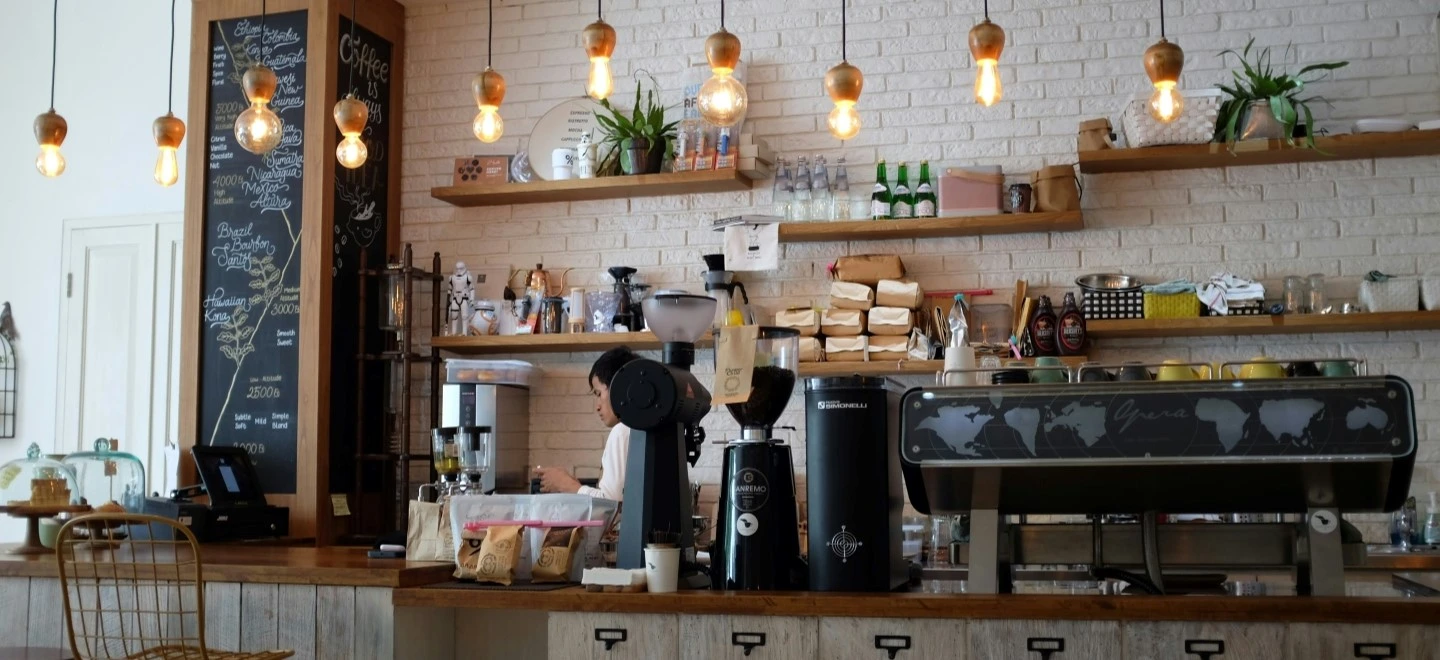 Comptoir de café chaleureux avec barista, machine à espresso et suspensions lumineuses.