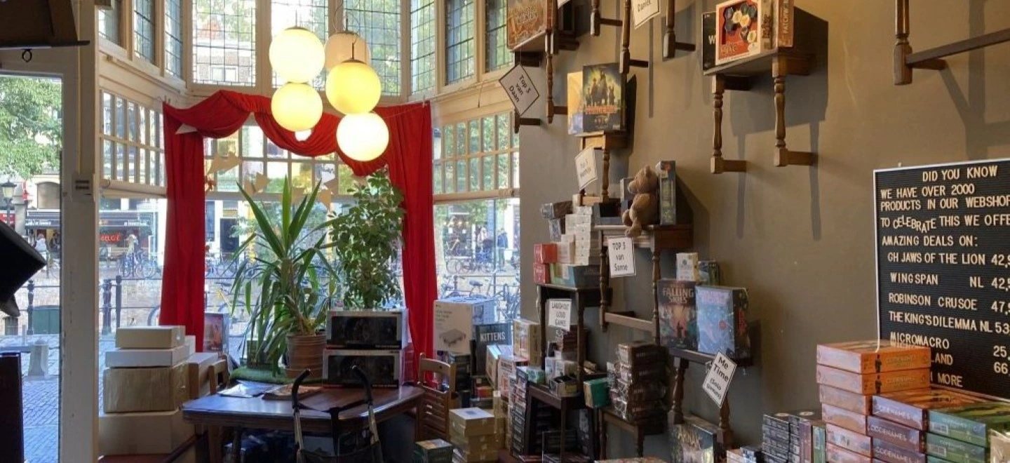 l'entrée de la boutique vue de l'interieur avec rideaux rouges, suspensions et jeux de société sur des étagères