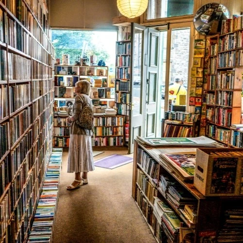 une femme dans une librairie face à une grande selection de livres