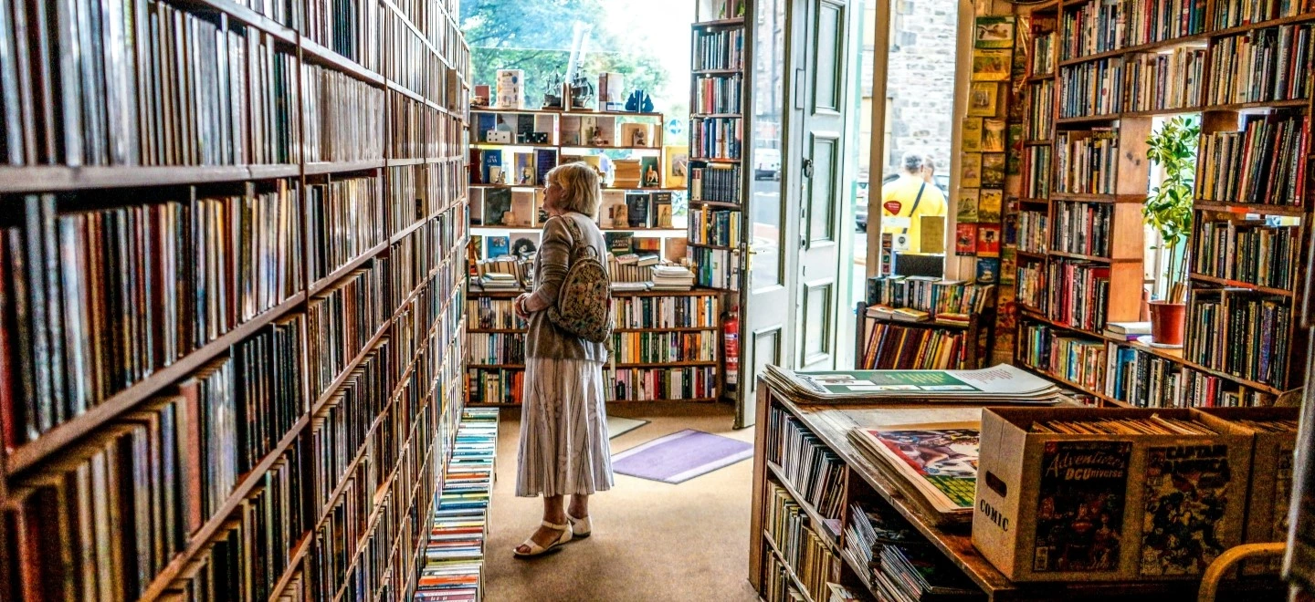 une femme dans une librairie face à une grande selection de livres